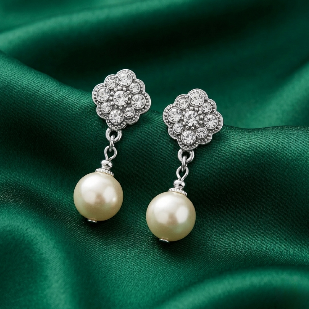 Faux pearl earrings with silver tone and crystal floral tops on a green satin background