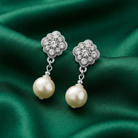 Faux pearl earrings with silver tone and crystal floral tops on a green satin background
