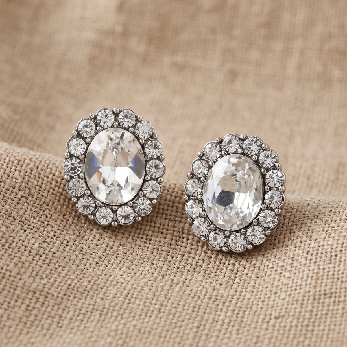 Crystal Oval Button Earrings resting on tan linen