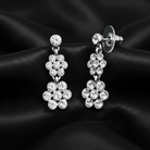 Silver crystal dangle earrings on a black satin fabric. 