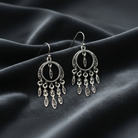 Silver earrings with dangling charms on a dark fabric background
