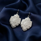 Ornate silver medieval shield earrings on a dark blue fabric background