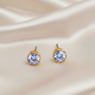 Light blue crystal stud earrings on a white fabric background.