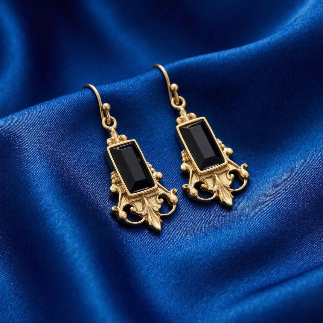 Gold earrings with black stones on a blue fabric background