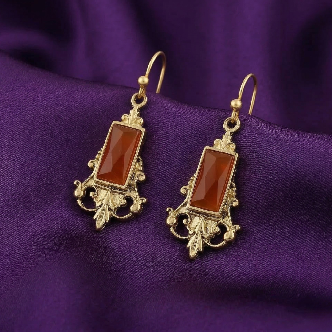 Pair of gold earrings with orange stones on a purple fabric background