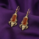 Pair of gold earrings with orange stones on a purple fabric background