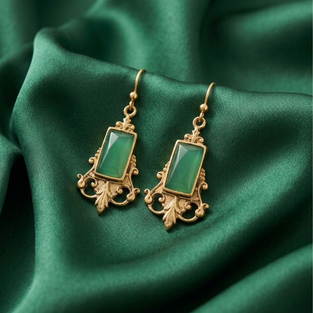 Gold earrings with green gemstones on a green fabric background