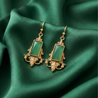 Gold earrings with green gemstones on a green fabric background