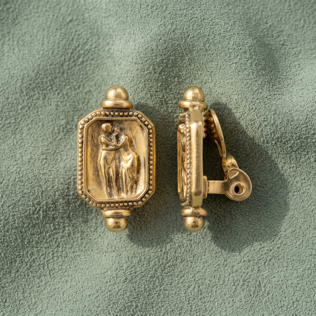 Antiquities Couture Gold Octagon Adoration Clip On Earrings resting on sage green suede. 