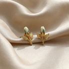 Gold earrings with porcelain rose design on a beige fabric background