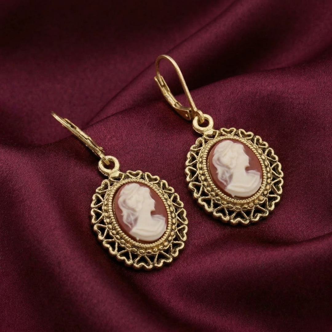 Gold earrings with cameo design on a maroon fabric background