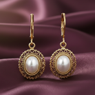 Gold earrings with faux pearl stones on a purple fabric background. 