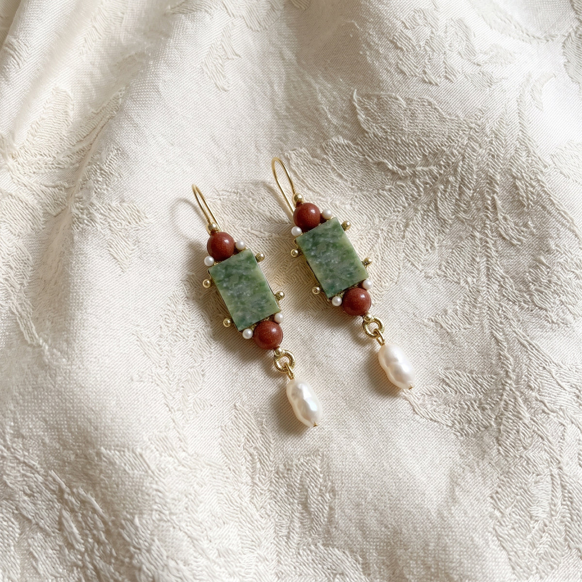 Antiquities Couture Roma Green Aventurine Gemstone Faux Pearl Museum Dangle Earrings displayed on a textured cream fabric background.