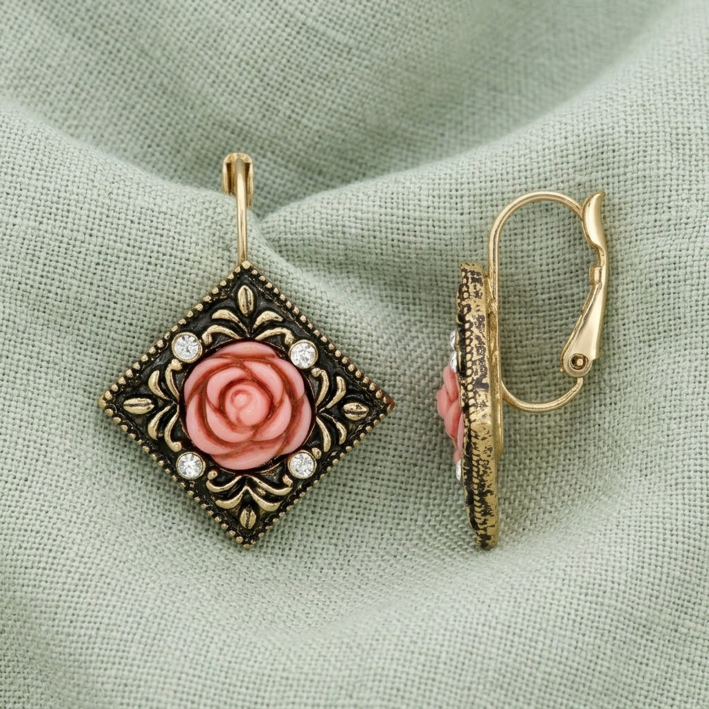 Pink Carved Rose With Crystal Accents Diamond-Shape Drop Earrings resting on light green linen