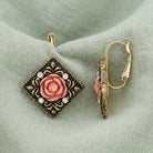 Pink Carved Rose With Crystal Accents Diamond-Shape Drop Earrings resting on light green linen