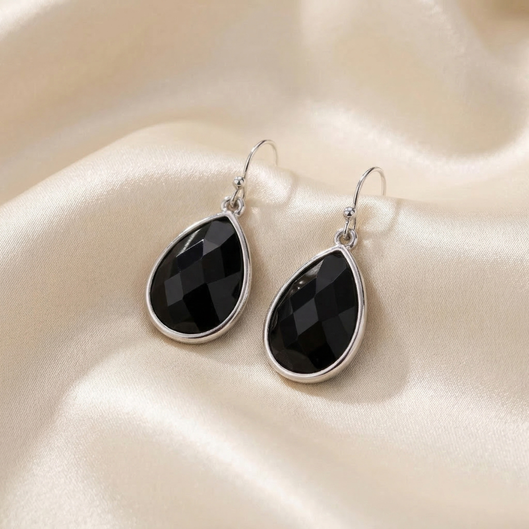 Black teardrop earrings on a beige satin surface