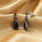 Pair of black teardrop earrings on a gold fabric background