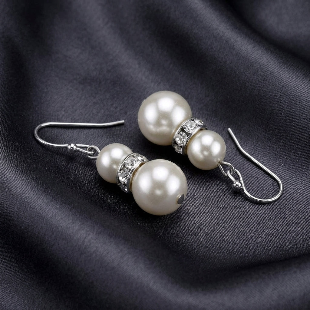 White faux pearl beaded earrings with clear crystal accents resting on dark satin fabric 
