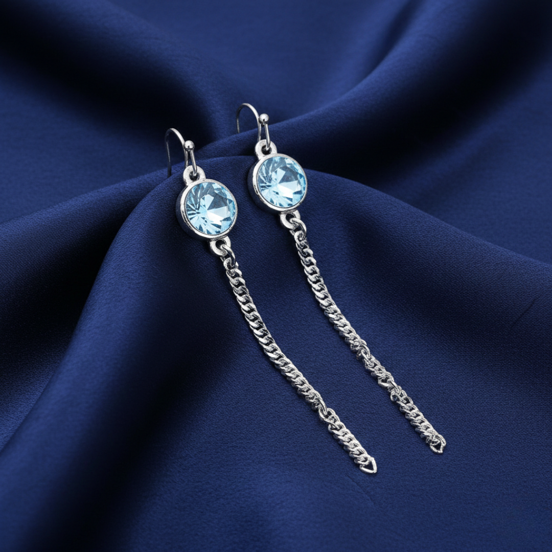Silver earrings with light blue crystals on a dark blue fabric background