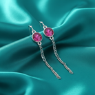 Silver earrings with pink crystals on a teal satin background