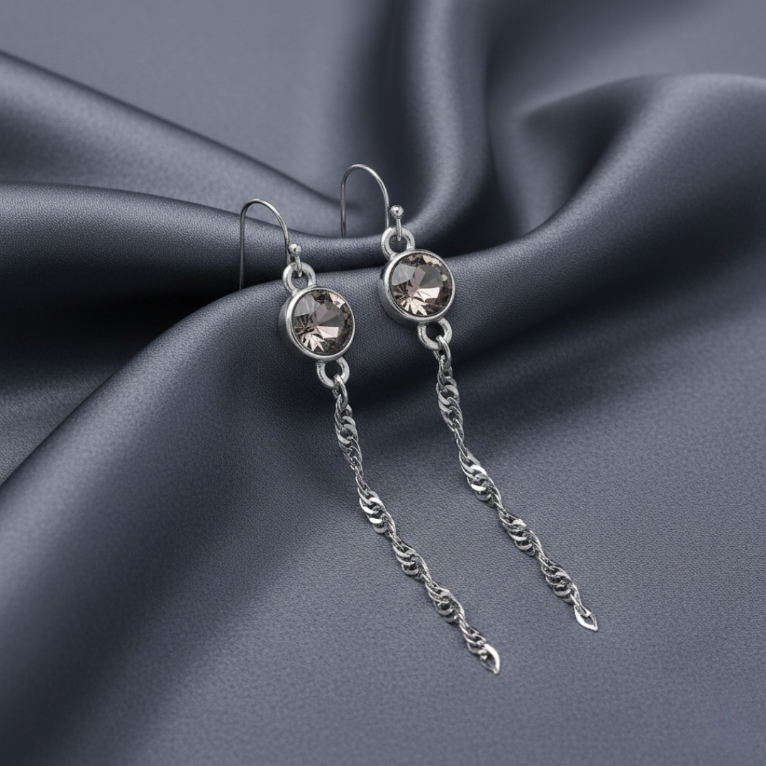 Silver earrings with chain details on a dark fabric background