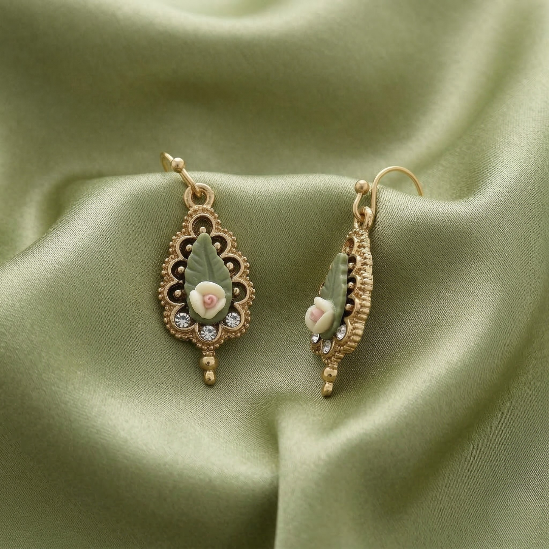 Decorative earrings with floral porcelain rose designs on a green fabric background
