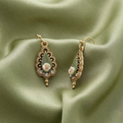 Decorative earrings with floral porcelain rose designs on a green fabric background