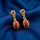 Pair of gold and red earrings with over 100 crystals and an egg-shaped design on a blue fabric background