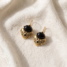 Antiquities Couture Black Corinthian Sculpted Heart Drop Earrings resting on white laced fabric