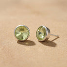 Petite Light Green Austrian Crystal Stud Earrings resting on smooth sand surface