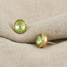 Round Sparkling Light Peridot Green Stud Earrings resting on beige linen