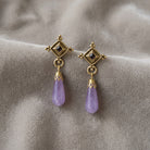 Antiquities Couture Purple Amethyst Teardrop Gemstone & Crystal Post Drop Earrings resting on greige velvet fabric