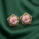 Pair of gold earrings with pink floral designs on a green fabric background
