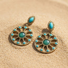 Pair of gold and turquoise earrings on a sandy background