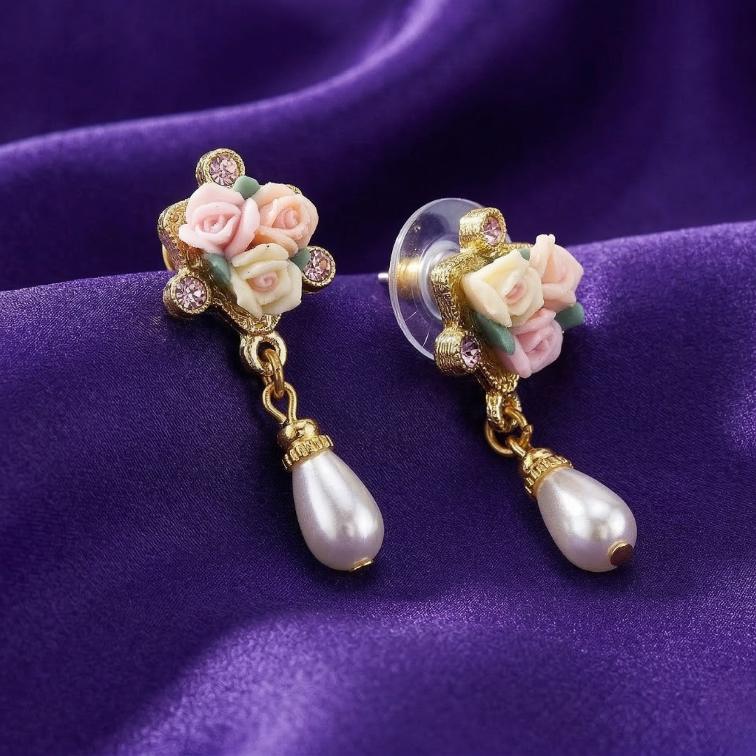 Decorative earrings with porcelain rose designs and faux pearl drops on a purple fabric background