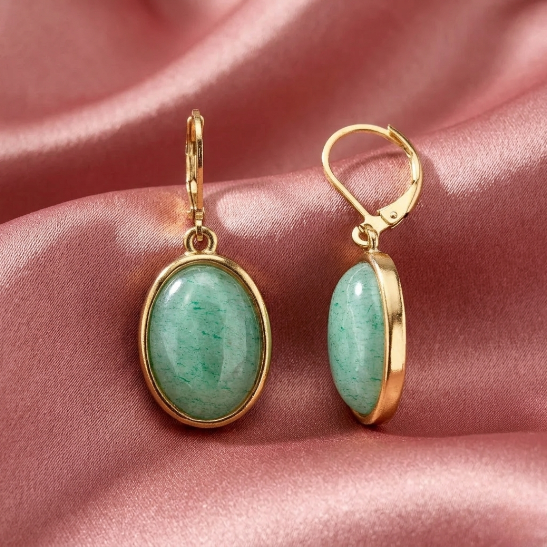 Gold earrings with green stones on a pink satin background