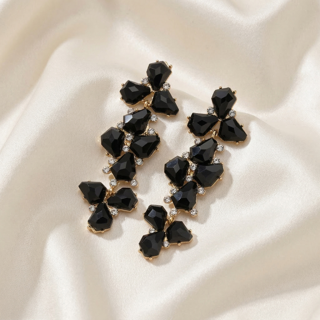 Black enamel gemstone earrings on a beige fabric background