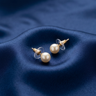Pearl earrings with gold posts on a blue fabric background