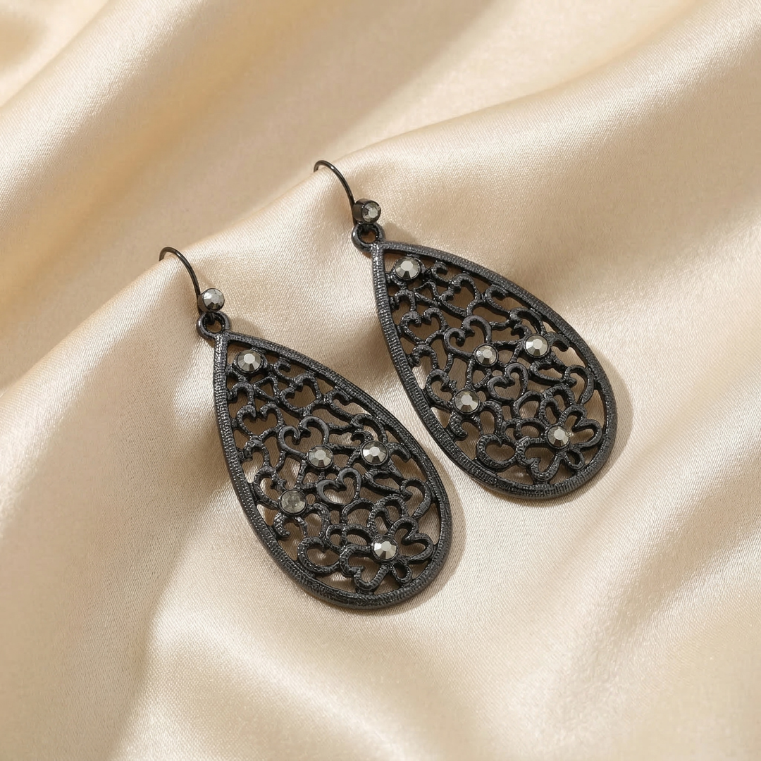 Pair of black filigree teardrop earrings on a beige fabric background
