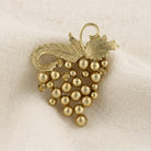 Gold tone faux pearl wine grape brooch pin resting on white linen