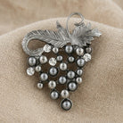 Gray faux pearl wine grape pin resting on beige linen