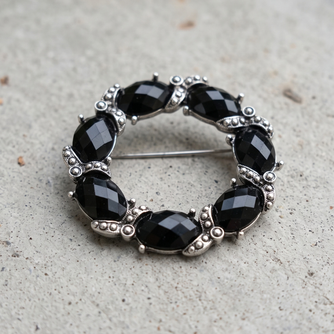 Black Faceted Stone Wreath Pin, photographed on a textured light gray surface.