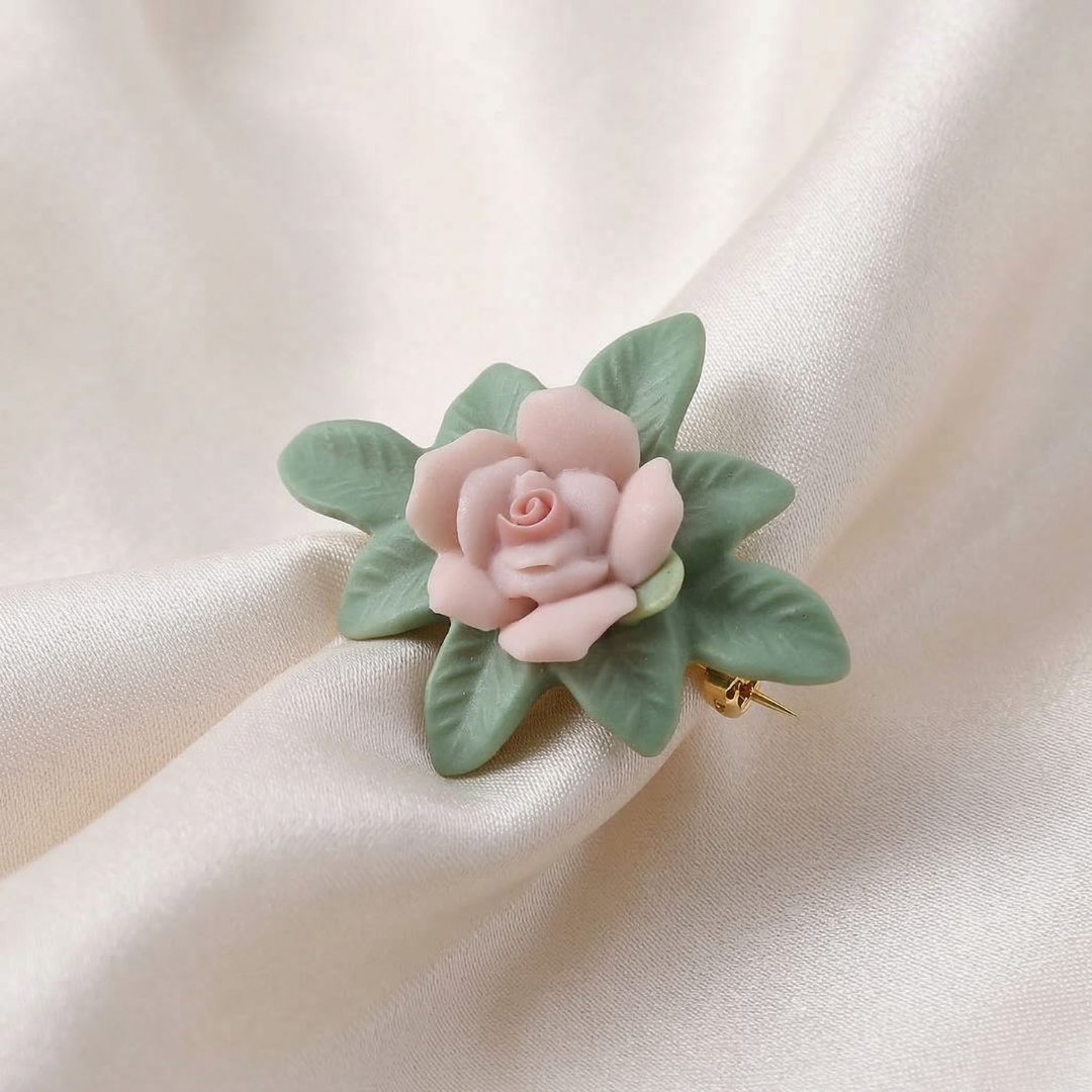 Floral brooch with pink porcelain rose and green leaves on a beige fabric background