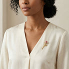 Woman wearing a white blouse with a porcelain rose floral-shaped brooch on a neutral background