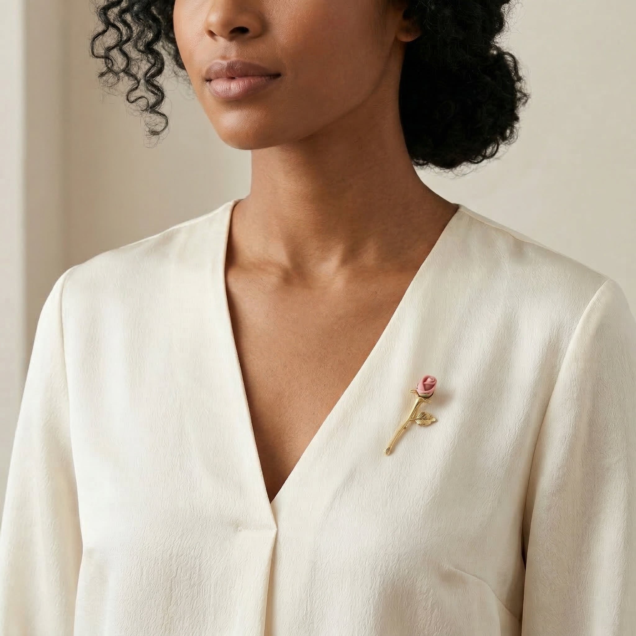 Woman wearing a white blouse with a porcelain rose floral-shaped brooch on a neutral background
