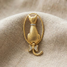Gold tone Backwards Cat Crystal Pin resting on beige linen