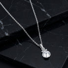A silver chain necklace with a round clear crystal pendant, displayed on a black marble surface.