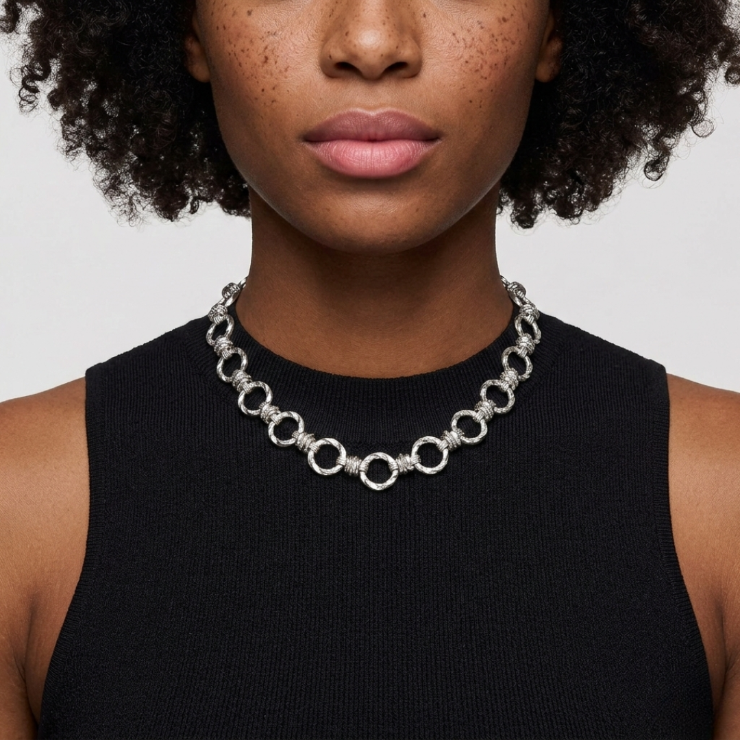 Person wearing a silver tone choker chain necklace against a neutral background