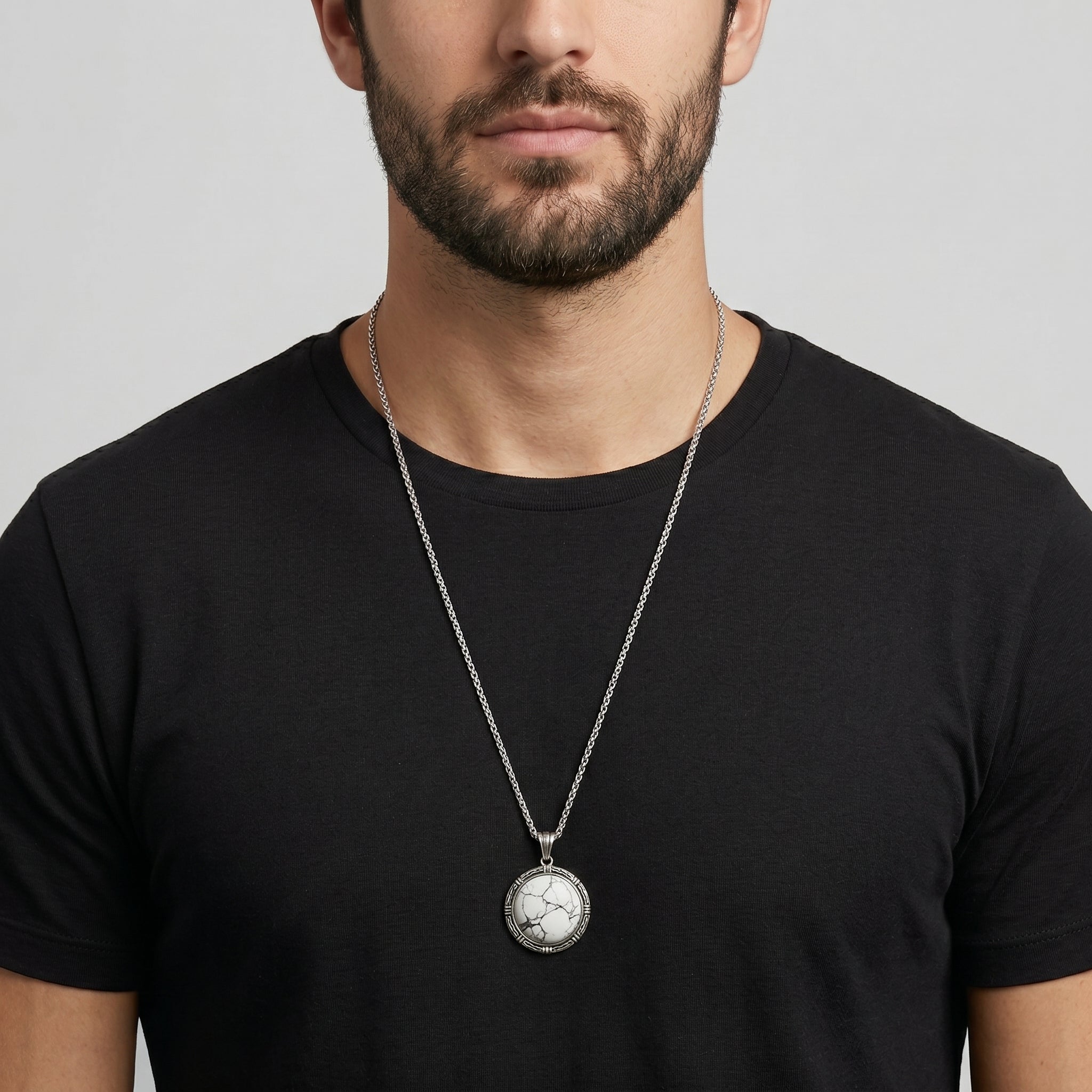 Man wearing a black t-shirt with a silver necklace featuring a round white stone pendant.