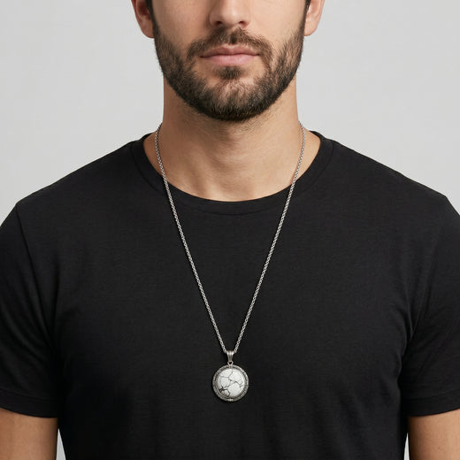 Man wearing a black t-shirt with a silver necklace featuring a round white stone pendant.